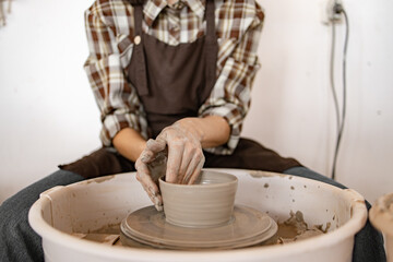 Female potter creating ceramic dish on potter's wheel using hands. Close-up of pottery process highlighting craftsmanship and creativity.