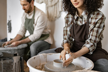 Man and woman working together creating pottery using clay on potter's wheel in a studio.