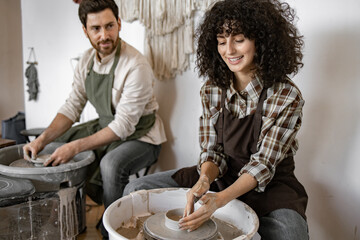 Man and woman potters working together on pottery wheel to create clay vases. They enjoy creating art and craft in studio.