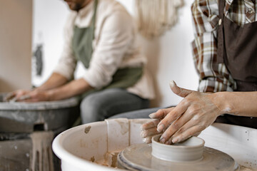 Man and woman working together on potters wheel creating clay pottery. Hands shaping clay vase in artistic studio. Creativity, craftsmanship, and teamwork.