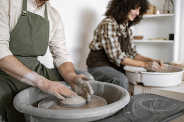 Man and woman potters shaping clay on potter's wheel in studio. Creative process, craftsmanship, and handmade pottery.