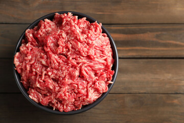 Raw ground meat in bowl on wooden table, top view. Space for text