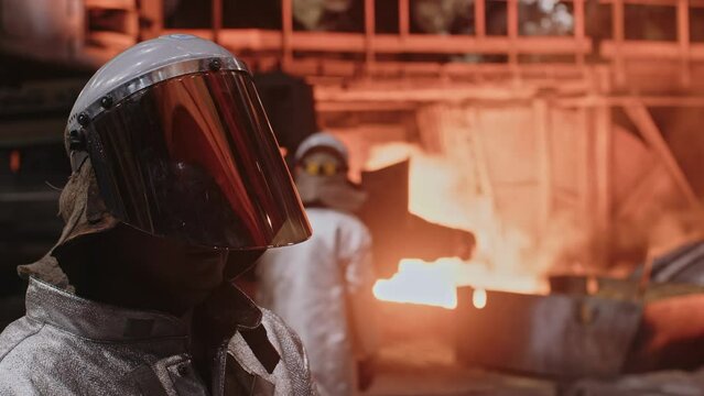 A man in a fireproof suit stands in the smelting shop of a metallurgical plant.