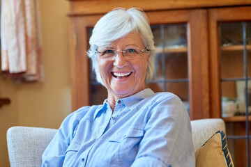 Portrait, laugh and senior woman on sofa for retirement, joke and glasses in living room. Funny,...