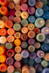 An abundant collection of small candles in various colors and shapes, tightly arranged to fill the entire frame. The candles display a range of hues from pastel to bright.
