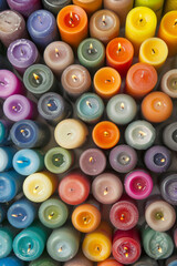 An abundant collection of small candles in various colors and shapes, tightly arranged to fill the entire frame. The candles display a range of hues from pastel to bright.