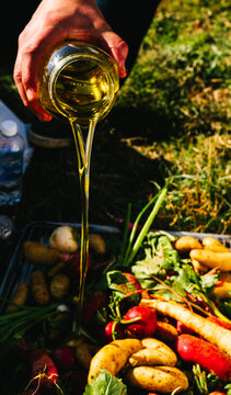A hand pours a sugary syrup onto a tray of vegetables to be roasted in an outdoor fire pit