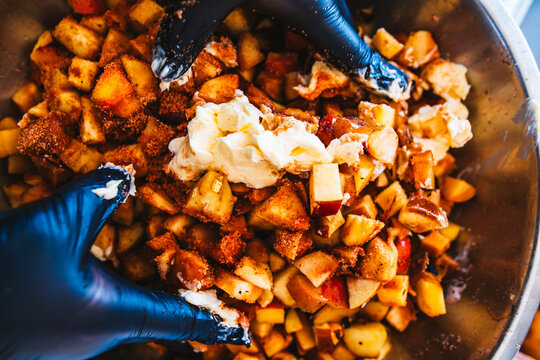 gloved hands mix smoked apples, butter, bourbon and spices in a stainless steel bowl
