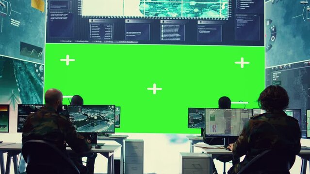 Diverse group of privates operating on a big screen isolated display, looks at a greenscreen and gathering intelligence to help with military operations in command center. Army facility base. Camera B