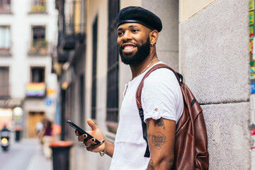 Stylish black man walking on the city street using smartphone