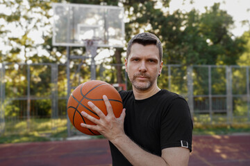 Man with basketball ball on court posing, looking at camera           
