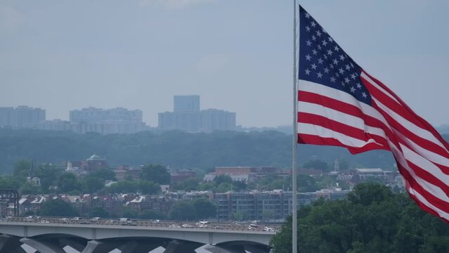 American Flag waves in slow motion in front of a cityscape and bridge