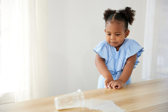 little African girl spilling milk and feeling sad on the table