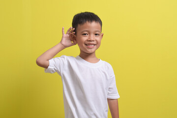 Image of Asian child trying to hear you listening attentively isolated on yellow background. portrait of an Asian boy posing cute and happy.