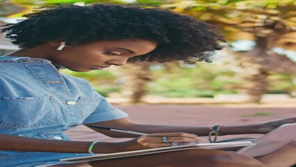 Girl learning online lesson making notes in copybook at street close up vertical