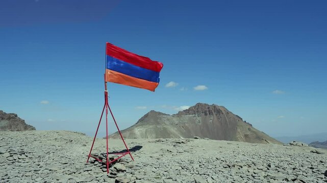 Shiny Armenian flag flutters in wind on summit peak of Mount Aragats