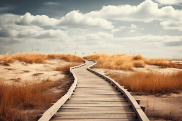 Wooden walkway leading to sandy beach with tall grass and cloudy sky.