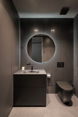 Illuminated round mirror in a dark bathroom interior