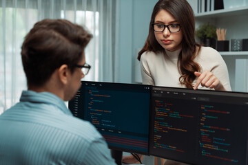 Woman colleague standing opposite to man programmer working on desk to discuss coding website...