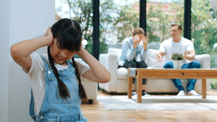Stressed and unhappy young girl huddle in corner, cover her ears blocking sound of her parent...
