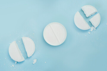 round tablet was divided equally. White broken pills lie on a blue background.