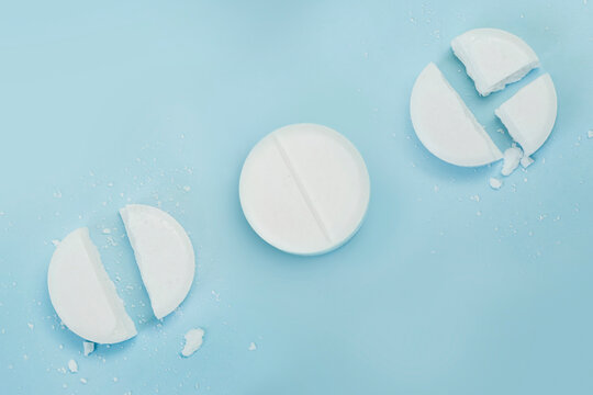 round tablet was divided equally. White broken pills lie on a blue background.