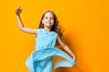 Joyful little girl in a blue dress leaping high in the air against a vibrant orange background