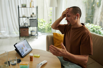 Worried man complaining about severe headache when video calling his doctor