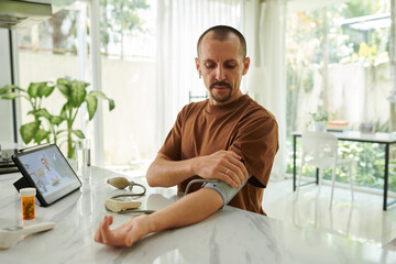 Man suffering from hypertension measuring blood pressure at home