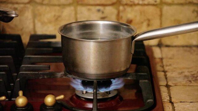 Rustic kitchen scene: a cast-iron pot filled with bubbling water, steam billowing from the surface, placed over a glowing gas stove burner. Cozy countryside ambiance. Front shot.