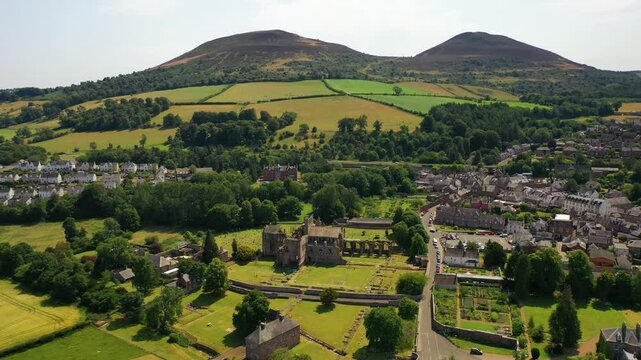 Aerial shot forward of beautiful countryside town of Melrose and bright green and yellow fields during spring in the Scottish Borders showing rural landscapes near Edinburgh, Scotland, United Kingdom