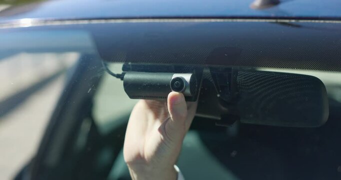 A hand adjusts the camera of a dash cam attached to a vehicle windshield