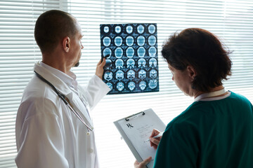 Doctor examining brain computer tomography scan and asking nurse to write out prescription
