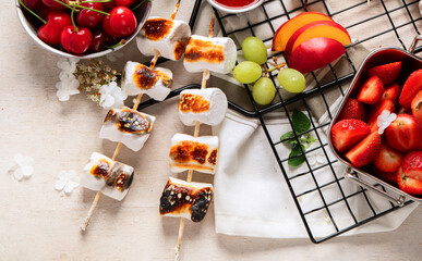 Marshmallow skewers and and strawberry, cherry, grame on light wooden background. Summer party food