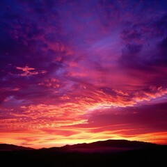 Fototapeta premium Stunning sunset with vibrant colors lighting up the sky over a silhouette of mountains, creating a mesmerizing natural landscape scene.