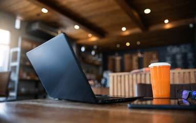 Comfortable workplace on wooden table with ice coffee cup, mobile phone and laptop, retro style cafe background