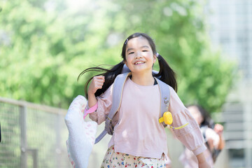 Cute girl running and posting with her school bag on her back against a beautiful fresh green...