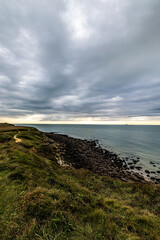 Naklejka premium Dramatic sky over a coastal cliff, rocky shore, and ocean view, showcasing wild beauty in this serene landscape