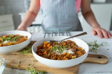 Homemade food. Delicious lentil stew on kitchen counter served by a woman with apron