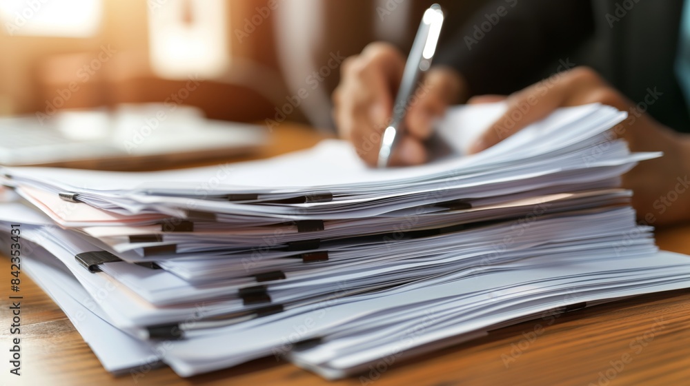Poster the image shows a close-up of a large pile of papers with a person's hands writing in the background