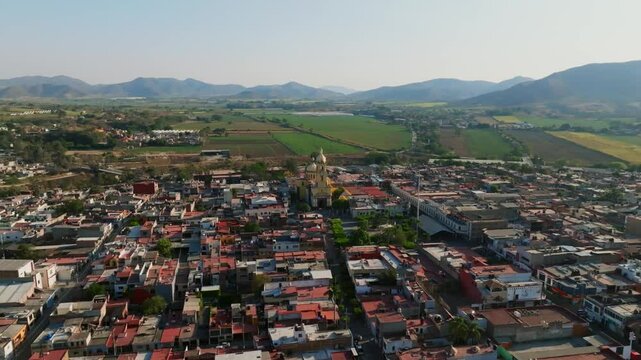 Panoramic aerial orbit of Tamazula city center with the main church, farm fields and distant mountains. Jalisco, Mexico