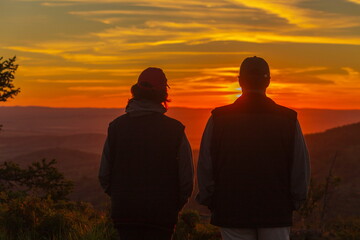 Fototapeta premium two silhouettes of two tourists in love against the background of an evening sunset in the mountains