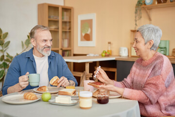 Portrait of happy senior couple enjoying breakfast together in cozy kitchen and smiling looking at each other