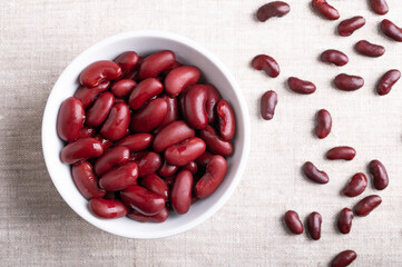 Kidney beans in a white bowl on linen fabric. Cooked and canned common kidney beans, a variety of the common bean Phaseolus vulgaris, a vegetarian staple food. On the right side dried uncooked beans.