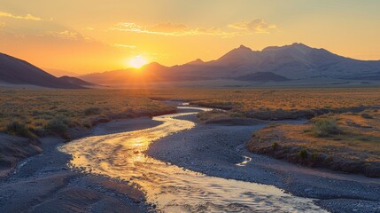 Dry riverbed meandering through a desolate desert landscape, with distant mountains silhouetted by the warm glow of the setting sun