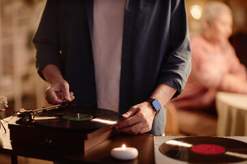 Front view close up of unrecognizable man setting up vinyl record player and enjoying retro music with ambiance copy space
