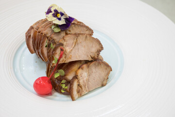A plate featuring a savory pork dish garnished with a single cherry.