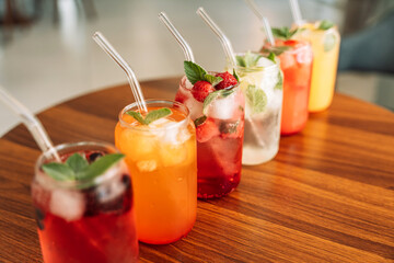 Fruit drinks with berries and ice in glass glasses and straws on a wooden table.