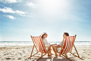 Couple, relax and beach chairs with umbrella on sand for vacation, holiday or weekend break....