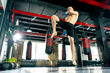 Obraz premium in a boxing fight club bald young boxer with tattoos in blue bandages trains a kick before a fight professional training fighting technique training